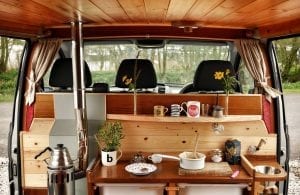 The inside of a selfbuilt campervan including diesel heater, mugs, saucepans and plants looking over into the front cab