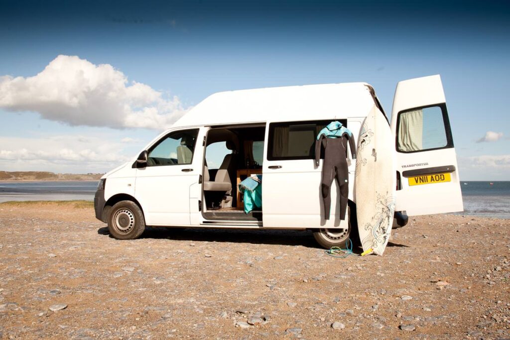 White campervan with wetsuit and surfboard on a beach