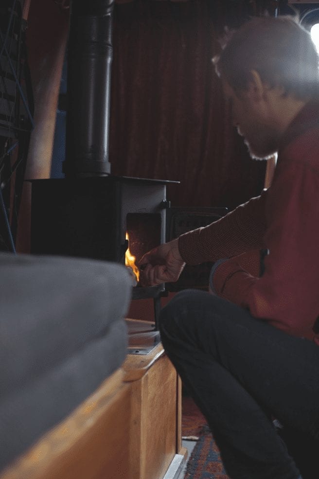 A man putting wood in a wood burner in a campervan