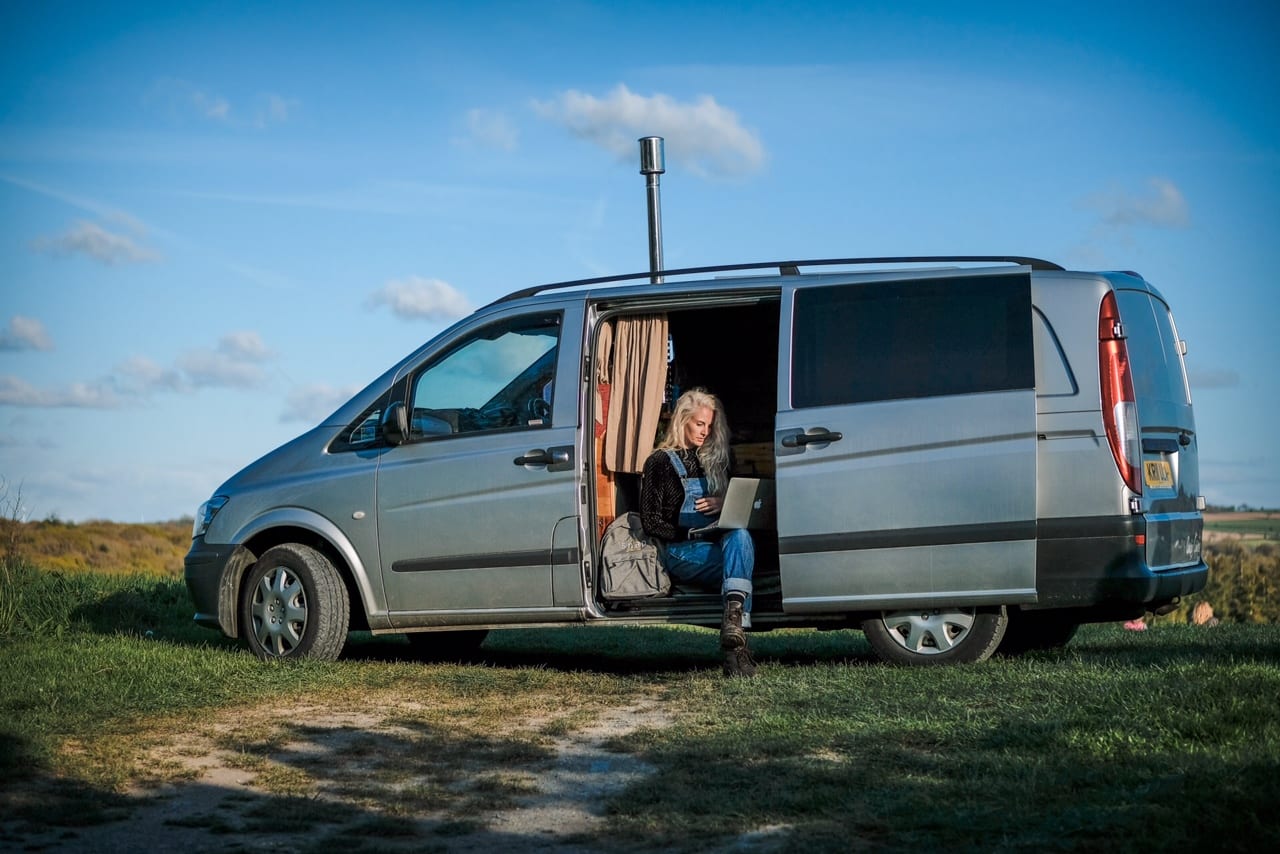 A woman working on her laptop sat on the step of a Mercedes campervan