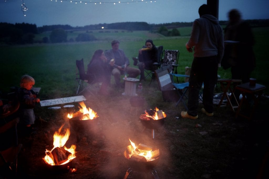 a group of people sat around campfires at a campervan festival