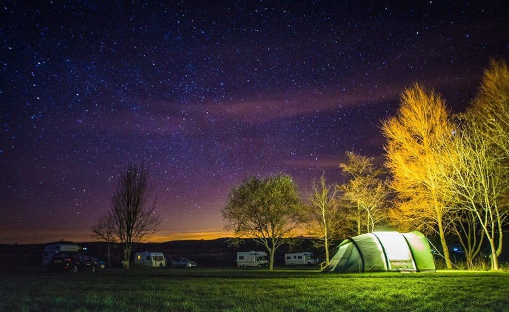 A starry night on a campsite with a tent and some campervans