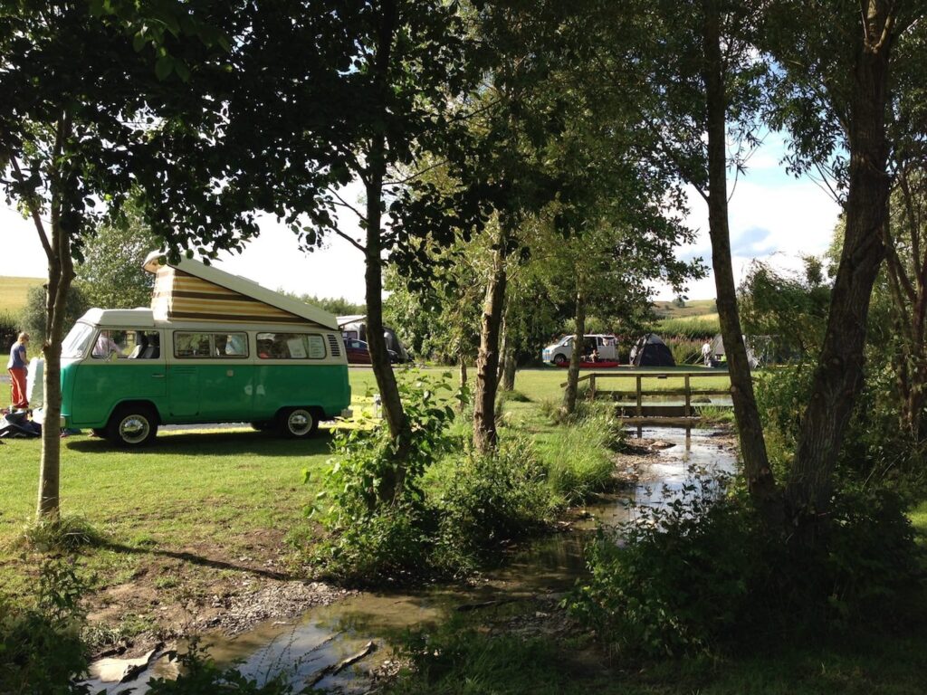 A campervan parked in a campsite with a small stream in the trees