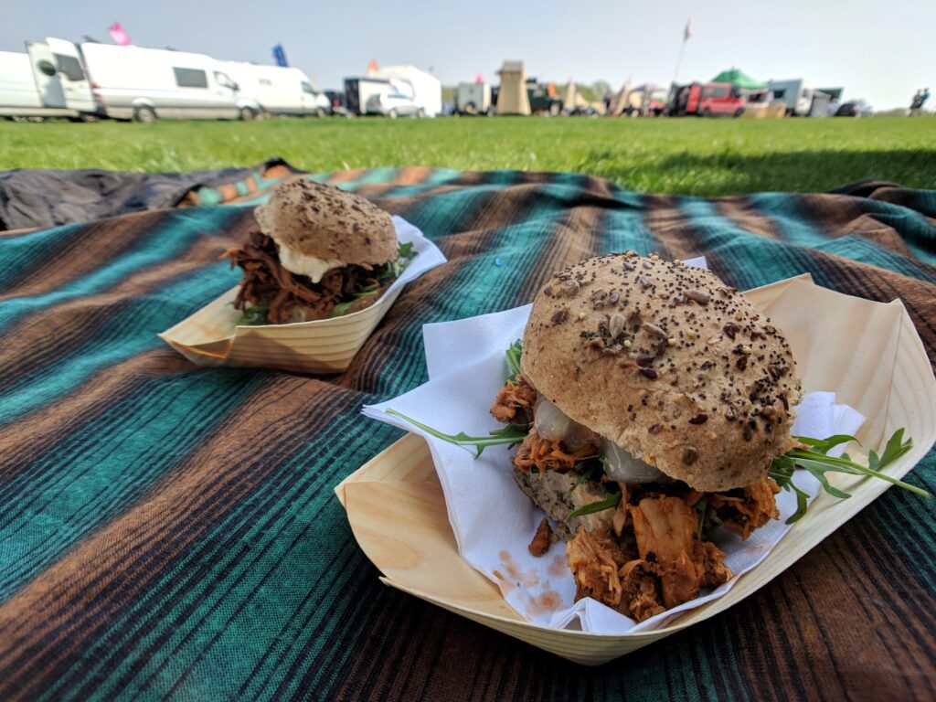 Two burgers on a picnic blanket in a campervan festival field