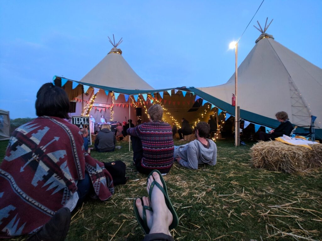 The Camp Quirky teepee with people sat outside and hay bales