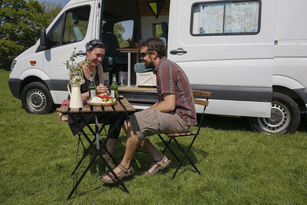 Man and woman sit outside their campervan at a picnic table