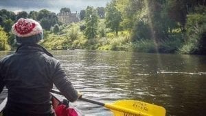 A woman in a bobble hat and coat canoeing down the Wye River