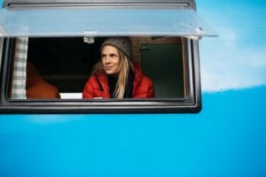 A lady in a red coat and winter hat looks out the window of a blue campervan