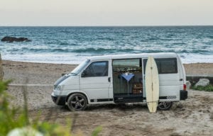 A campervan with surf board on the beach with the sea in the background