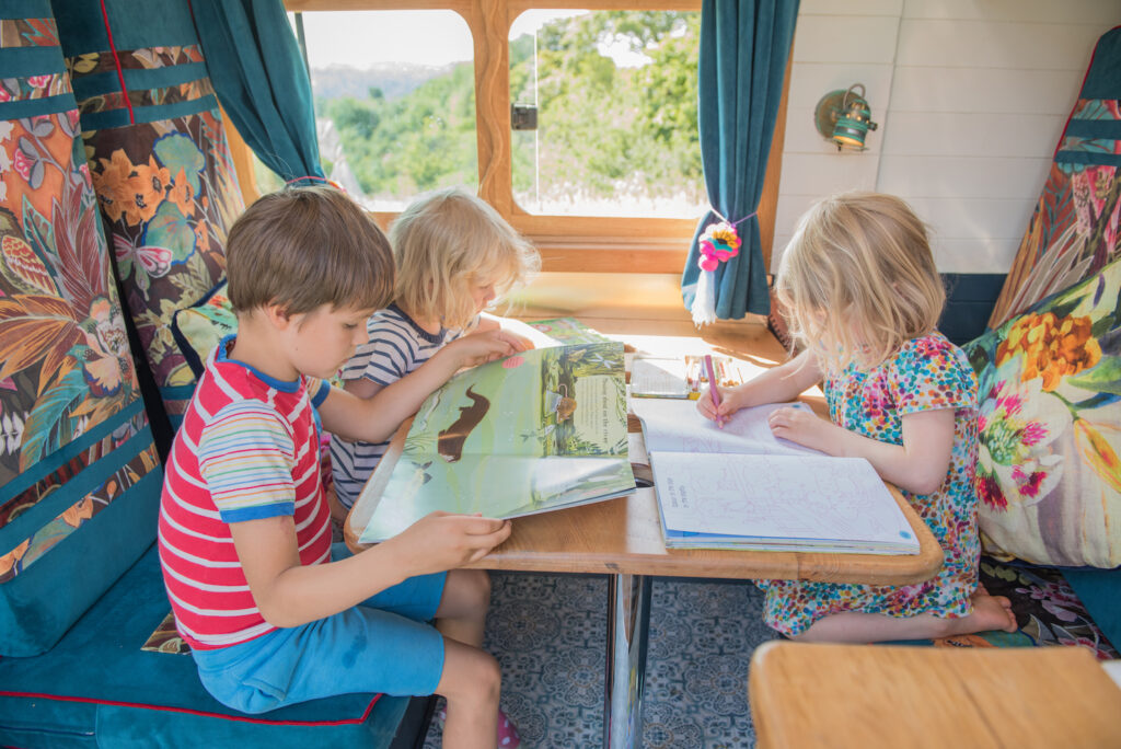 Children entertained in a campervan reading books and listening to audiobooks