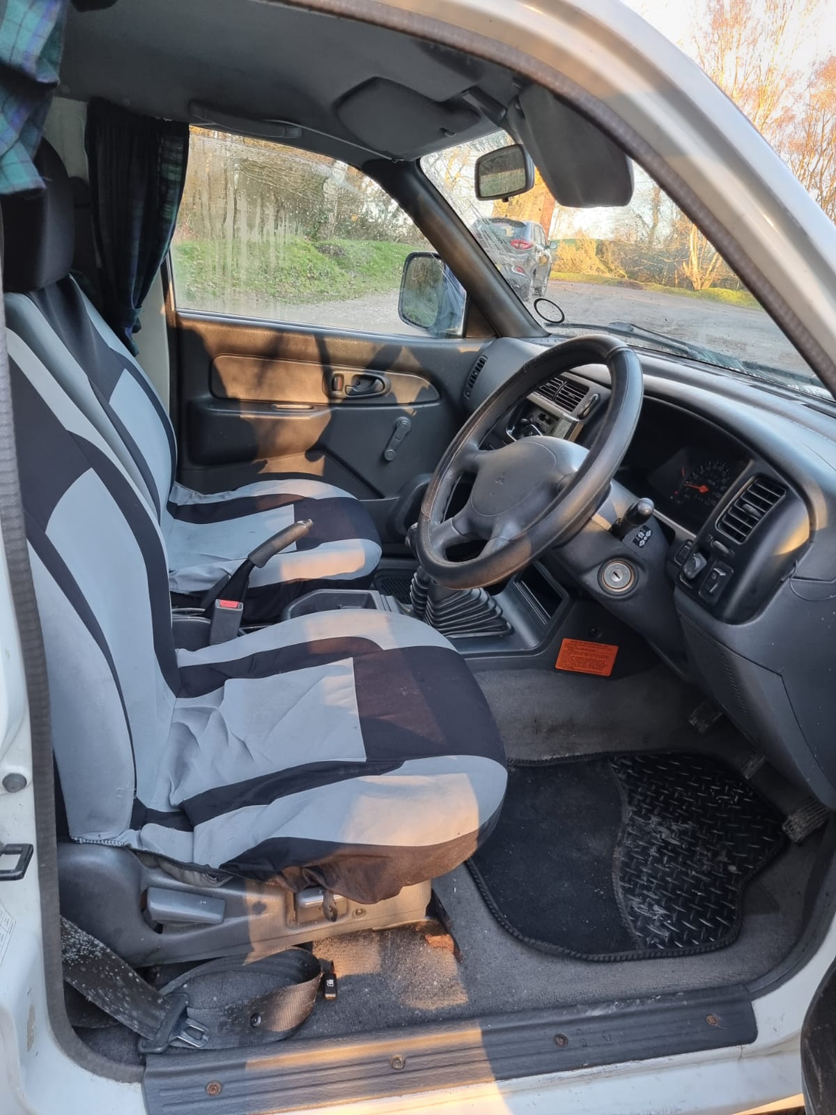 The image shows the interior of a car with grey and black seat covers on the front seats. The steering wheel is on the right side, indicating a right-hand drive vehicle. The dashboard contains various controls and a ventilation system. The interior appears clean and well-maintained.