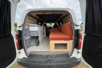 camper conversion with the back door open allowing you to see the seats and storage