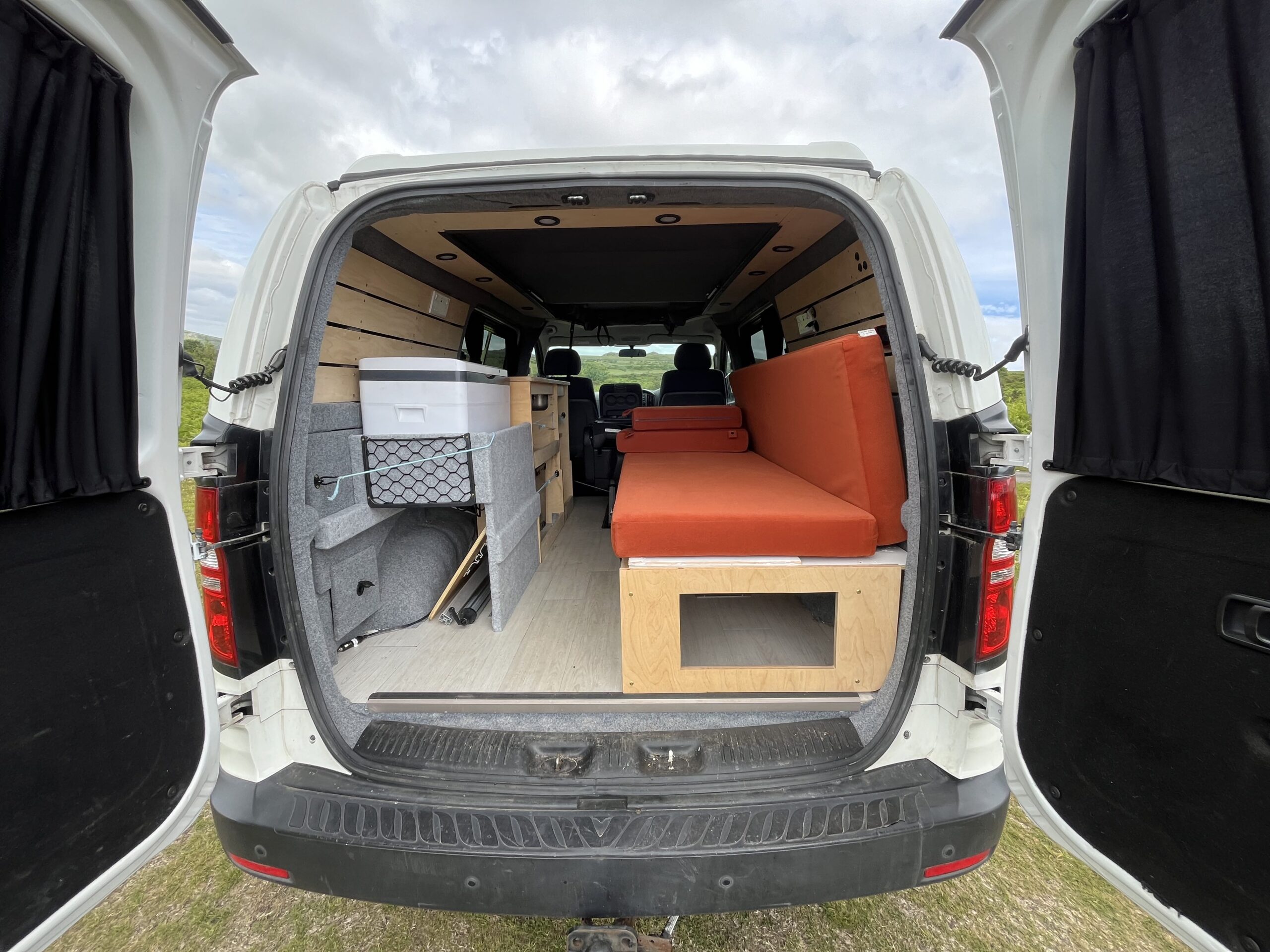 camper conversion with the back door open allowing you to see the seats and storage