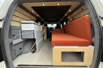 camper conversion with the back door open allowing you to see the seats and storage