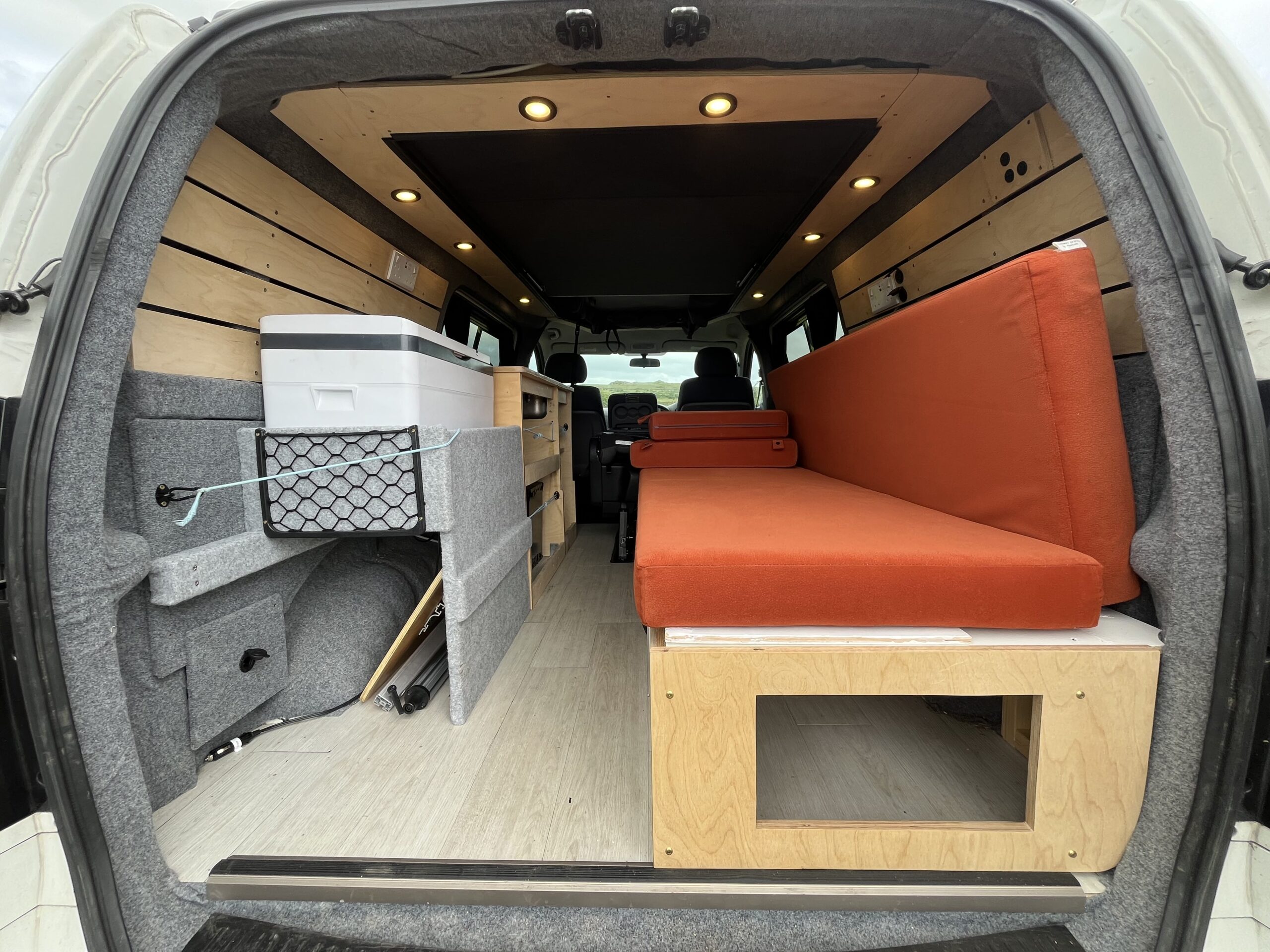 camper conversion with the back door open allowing you to see the seats and storage
