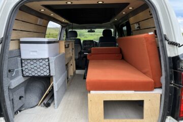 camper conversion with the back door open allowing you to see the seats and storage