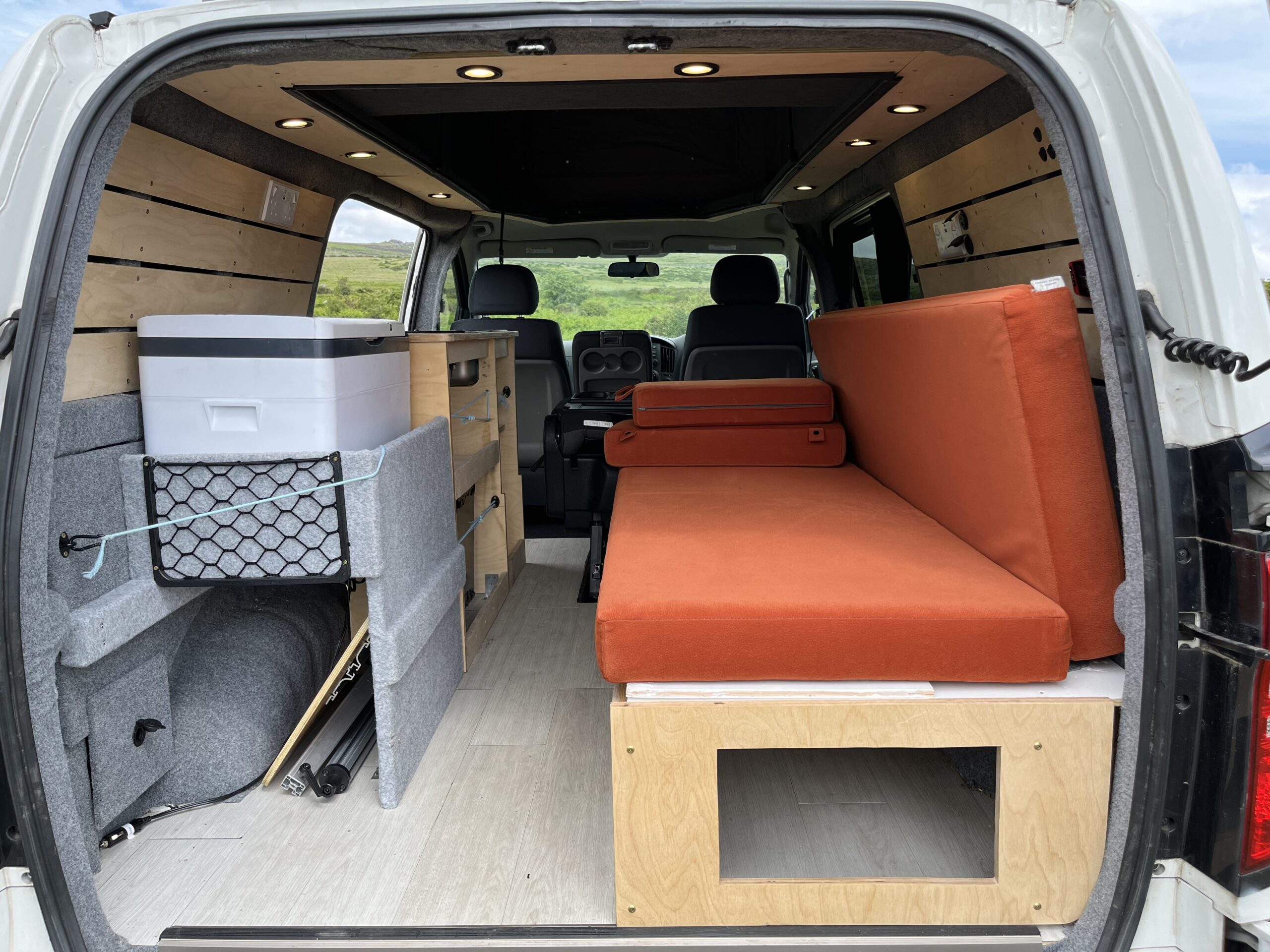 camper conversion with the back door open allowing you to see the seats and storage