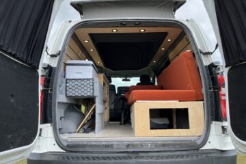 camper conversion with the back door open allowing you to see the seats and storage