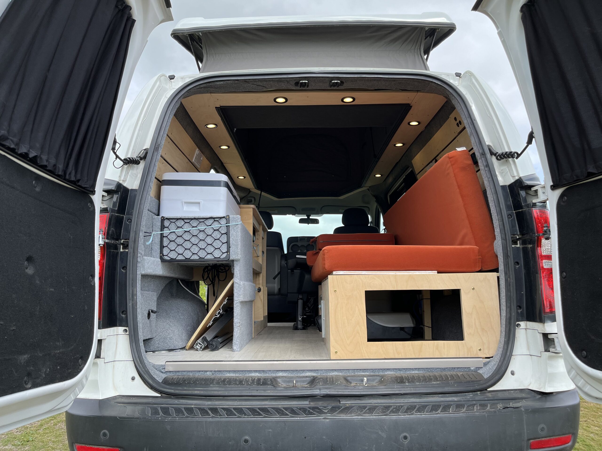 camper conversion with the back door open allowing you to see the seats and storage